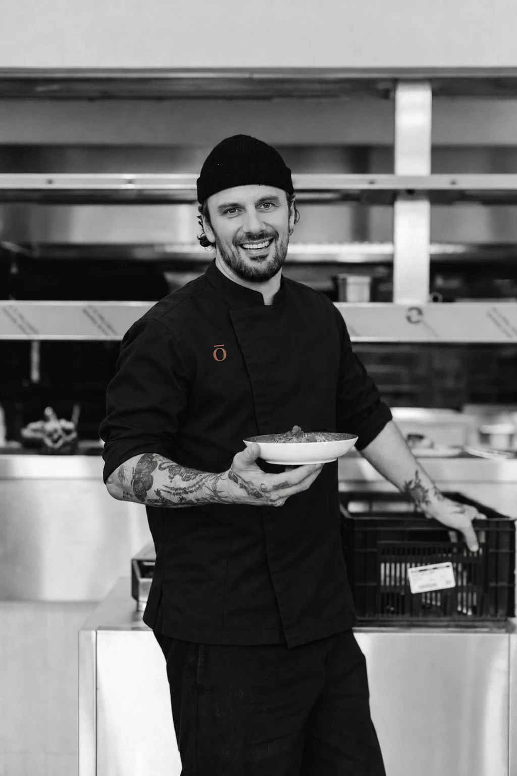 Een lachende kok met een bord in de keuken, in zwart-wit